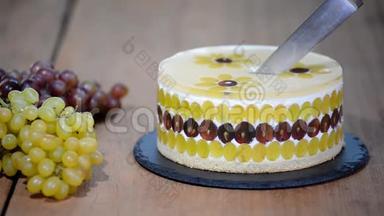 用刀子切慕斯蛋糕和葡萄。 用葡萄装饰的圆慕斯蛋糕